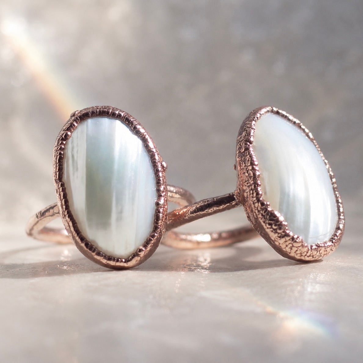 Two rings with copper bands and white pearl stones on a reflective surface.