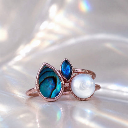 Ring with blue gemstones and a pearl on a white shell background