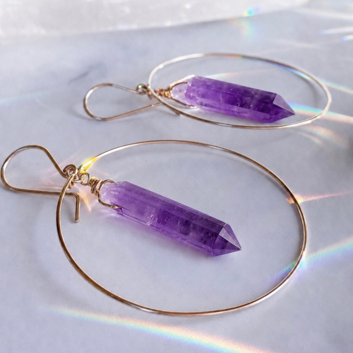 Purple crystal earrings with gold hoops on a white background