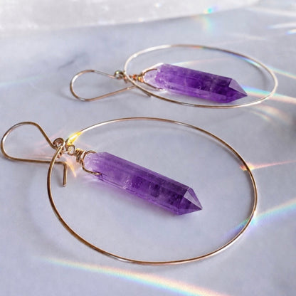 Purple crystal earrings with gold hoops on a white background