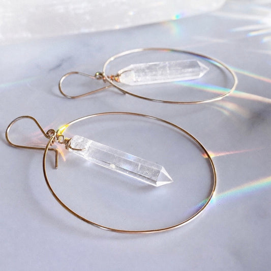 Gold hoop earrings with clear crystal pendants on a reflective surface