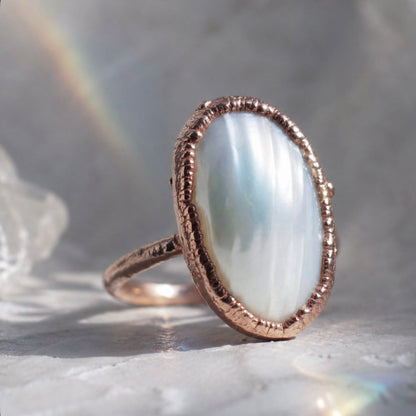 Copper ring with a large white stone on a marble surface