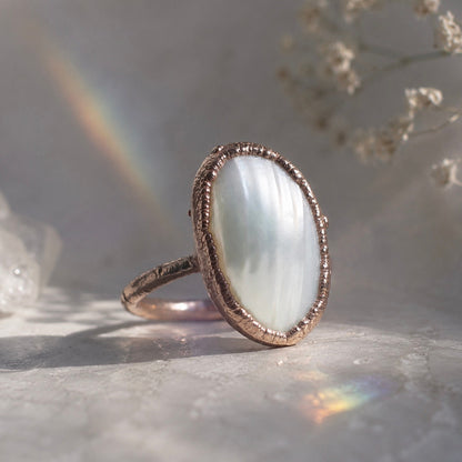 Ring with a large, oval stone on a textured surface with a blurred natural background