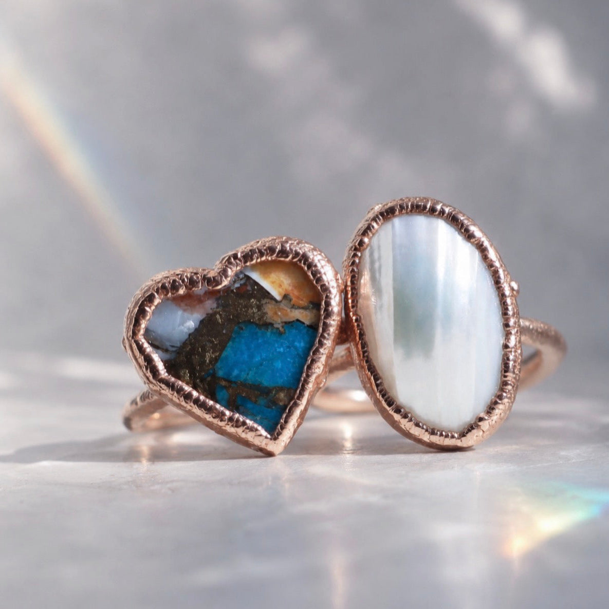 Two copper rings with embedded stones on a reflective surface