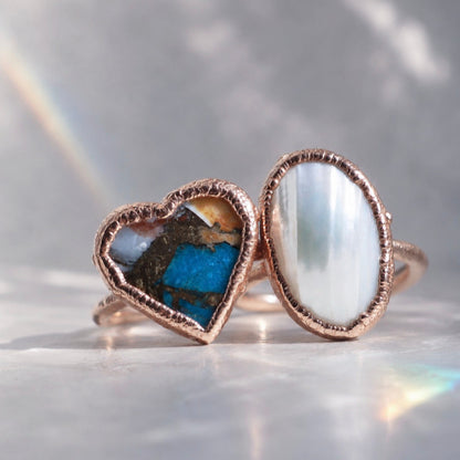 Two copper rings with embedded stones on a reflective surface